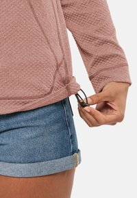 Top a maniche lunghe color rosa con texture e cordoncino regolabile all'orlo, abbinato a pantaloni shorts di jeans blu con risvolto.