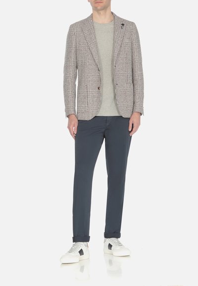 Blazer da uomo in un motivo a quadri marrone e bianco, abbinato a una t-shirt grigia, pantaloni blu navy e sneaker bianche con dettagli neri.