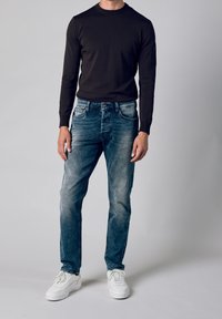 Czarna koszula z długim rękawem i okrągłym dekoltem, zestawiona z jasnoniebieskimi wyblakłymi jeansami i białymi trampkami, z subtelnymi detalami przeszyć na dżinsach.