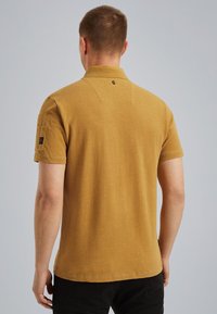 Polo tričko s krátkým rukávem v hořčicově žluté barvě, vyrobené z bavlněného směsového materiálu, disponuje límečkem, malým logem na zadní straně a kapsou na rukávu.