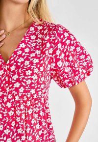Abito floreale rosa con piccoli fiori bianchi, maniche a sbuffo e vita arricciata. Realizzato in tessuto leggero con una finitura testurizzata.