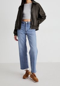 Tmavě zelená kožená bomber bunda, šedý krátký top, světle modré široké džíny a hnědé tenisky s bílými akcenty.