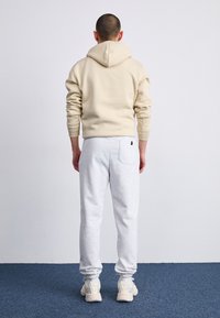 Beige bomullgenser med hette og snor, kombinert med lysegrå joggebukser med elastiske mansjetter og baklomme. Nøytrale fargetoner på fottøy.