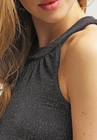 Top bez rękawów w ciemnym materiale z teksturowanym wzorem, charakteryzujący się zgromadzonym dekoltem i dopasowanym krojem w okolicy ramion.
