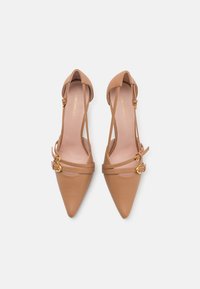 Zapatos de piel marrón claro con punta afilada y tiras en el tobillo, hebillas decorativas y una textura suave. Presentan detalles en dorado y un diseño minimalista.