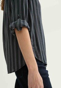 Black and white striped blouse with rolled sleeves, featuring a lightweight fabric and a slightly curved hem, worn with dark pants.