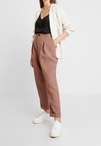 Rutig högmidjade byxor i rost och kräm med avslappnad passform, ihop med ett svart satinlinne och en texturerad krämfärgad kofta.