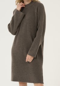 Brun rippad stickad klänning med hög halsringning och långa ärmar. Har en avslappnad passform och mjuk textur. Slutar strax ovanför knäet.