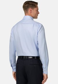 Gaiši zils krekls ar garām piedurknēm, pogu aprocēm, izkliedētu apkakli un smalku rūtiņu rakstu, kombinēts ar tumšiem svītrainiem biksēm.