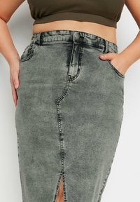 Kynskjørt i denim i falmet grått, med en frontslisse, sømdetaljer og sidelommer. Materialet har en myk tekstur med en svak glans.