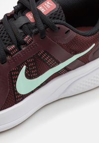 Nike-kengät, joissa on bordo verkkomateriaali, mustat yksityiskohdat, vaaleanvihreä swoosh-logot ja valkoinen pohja. Teksturoitu nauhoitus ja brändimerkki näkyvissä.