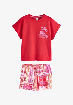 Czerwona koszula z krótkim rękawem z różowym nadrukiem palmy i zachodu słońca, zestawiona z szortami na elastycznym pasie zdobionymi czerwonymi, różowymi i pomarańczowymi wzorami geometrycznymi i słonecznymi.
