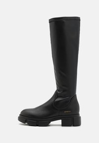 Knee-high black leather boot with minimalistic design, textured finish, block heel, and gold logo accent on the side.