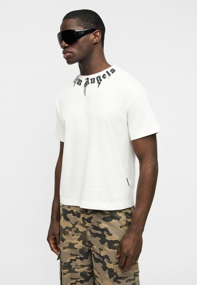 Λευκό κοντομάνικο t-shirt με μαύρο γραφικό "Los Angeles" στο λαιμό, συνδυασμένο με καμουφλαρισμένο παντελόνι cargo.