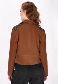 Brun faux læderjakke med et cropped design, der har teksturerede sorte accenter på skuldrene og lynlåse på manchetten.