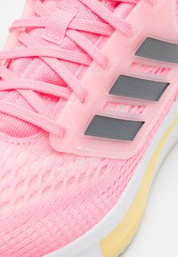 Vaaleanpunaiset urheilukengät, joissa on teksturoitu kangasvarsit, läpikuultavat yksityiskohdat ja harmaat kolmionauhat. Mukana kevyt pohja.