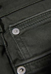 Donkergroen denim stof met een voorzak voorzien van een zilveren metalen knoop en contrasterend groene stiksel. Glad textuur met een lichte glans.