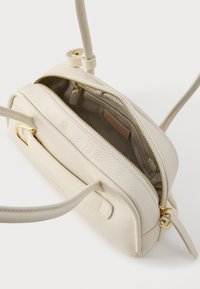 Gevoerd crèmekleurig leren tas met een ritssluiting, voorzien van gouden hardware en twee handvatten. De binnenkant is gemaakt van beige stof met een klein label.