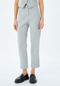 Helle graue, maßgeschneiderte Hose mit glatter Textur, hoch tailliert, mit gerafftem Vorderteil und verkürzter Länge. Kombiniert mit schwarzen Slippern.