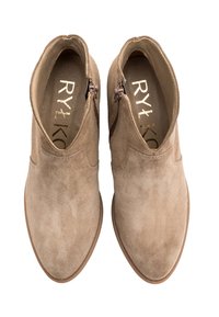 Para beżowych zamszowych botków za kostkę z bocznymi zamkami i złotym logo wewnątrz, widzianych z góry na białym tle.