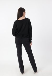 Zwarte gebreide trui met een losse pasvorm en wijde halslijn. Gecombineerd met donkere jeans, die een eenvoudig, monochroom ontwerp laat zien.