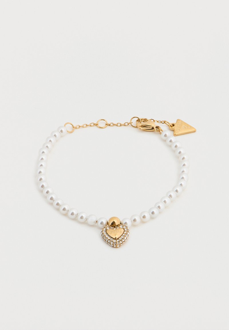 Βραχιόλι με λευκές πέρλες και χρυσή καρδιά ως κρεμαστό κόσμημα, διακοσμημένο με στράς. Διαθέτει κούμπωμα σε χρυσό χρώμα και προσαρμοζόμενο αλυσίδα.