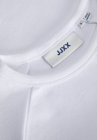 White ribbed T-shirt with a crew neckline. Features a "JJXX" label and a smooth, soft texture. Size tag visible on the inside.