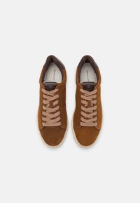 Braune Wildledersneaker mit beigen Schnürsenkeln, abgerundeter Spitze und kontrastierenden braunen Lederakzenten. Markenlogo im Inneren des Schuhs.