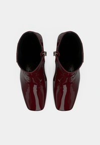 Bottines en cuir verni bordeaux avec un bout pointu élégant et des accents en métal argenté. Texture lisse, design épuré.