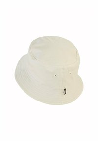 Beige cotton bucket hat with a wide brim, soft texture, round crown, and eyelets on the sides. Features a black adjustable drawstring.