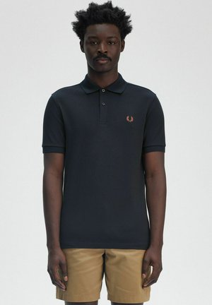 Polo shirt blu navy con colletto, tre bottoni e logo ricamato sul lato sinistro del petto; abbinato a pantaloni corti beige.