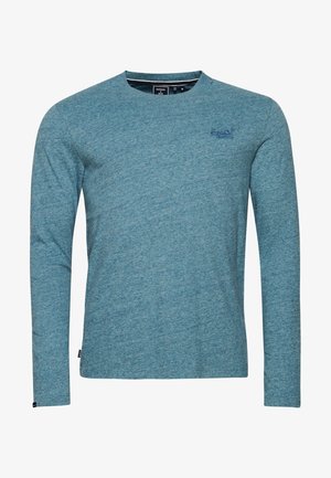 Blaues Langarmshirt mit Rundhalsausschnitt, dezent besticktem Logo auf der linken Brust und kleinem schwarzem Etikett nahe dem unteren Saum.
