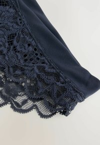 Marineblaue Stoffbekleidung mit kunstvollen Spitzenbesätzen, die florale Muster, gewellte Kanten und eine weiche Textur aufweisen. Nahaufnahme der Details.