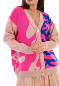 Stickad cardigan med rosa och blå abstrakta mönster, en beige kant och knapplås framtill. Mjuk textur, avslappnad passform.