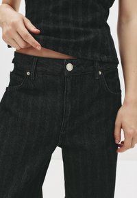 Jeans in denim nero con un sottile motivo a righe, tasche frontali e chiusura con bottone silver in vita. Tessuto morbido e texturizzato.