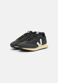 Tenis preto e verde oliva com materiais de rede e camurça, detalhes de logotipo brancos e sola de borracha texturizada. Design com atacadores.
