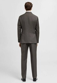 Gray suit jacket and pants made of textured fabric, with a tailored fit and a single vent on the jacket back. Black shoes complete the look.