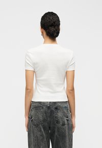 Λευκό κοντομάνικο t-shirt με εφαρμοστή γραμμή, σ ε συνδυασμό με ψηλόμεσα γκρι τζιν παντελόνια με δύο τσέπες στο πίσω μέρος και διακριτικό μπλε λογότυπο.