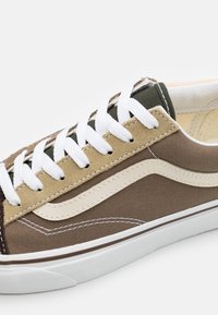 Tenisky s kombinací hnědé plátno a světlého semiše, bílé tkaničky a krémový boční pruh; gumová podrážka; vypolstrovaný límec; čisté švy.