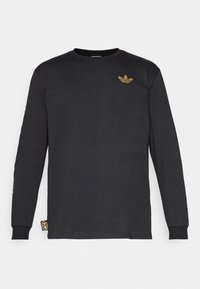 Camisa negra de manga larga hecha de algodón, con un logo bordado en dorado en el pecho y una etiqueta en el dobladillo. Textura suave, cuello redondo.