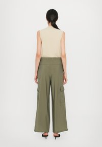 Beige top tanpa lengan dipadukan dengan celana cargo hijau zaitun berpotongan lebar yang memiliki saku samping besar dan tekstur yang halus. Desain minimalis.