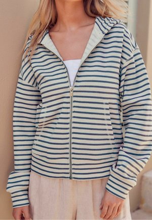 Pruhovaná mikina na zip v světlé smetanové a námořnické barvě, s předním zipem, dvěma kapsami a kapucí; vyrobena z měkké tkaniny s volným střihem.