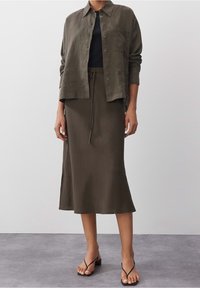 Oliivinvihreä pellavapaita, musta kapea toppi ja pitkä oliivinvihreä hame, jossa on kiristysnyöri vyötäröllä, sivuhalkio ja yksinkertaiset mustat sandaalit.