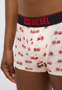 Ανδρικά εσώρουχα με ανοιχτό ροζ ύφασμα διακοσμημένο με σχέδιο κερασιών. Μαύρη ελαστική ζώνη μέσης με το λογότυπο "DIESEL" σε κόκκινο χρώμα. Μαλακό, ελαστικό υλικό.