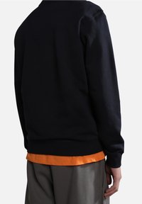 Sudadera navy con un escote redondo, puños y dobladillo acanalados. Una camiseta naranja asoma por debajo, combinada con pantalones grises.