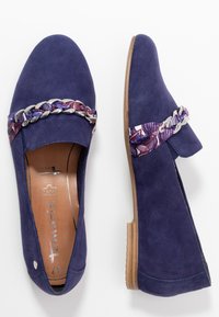 Chaussures en daim bleu marine avec un bout arrondi, présentant une sangle tressée à motif floral et un accent métallique. Semelle en bois plate, élastique sur les côtés pour un bon ajustement.