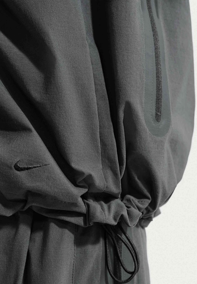 Dark grey fabric with an elastic drawstring cinch and a small black embroidered Nike logo near the bottom left.