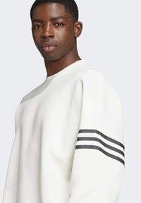 Sweat-shirt blanc avec trois rayures noires horizontales sur la manche gauche. Design à col rond avec une texture douce et lisse.