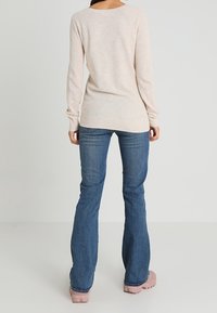 Pull en maille beige à manches longues, col rond et finition texturée, associé à un jean évasé bleu et des chaussures roses.