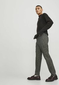 Maglione nero con texture, dotato di scollo a costine, abbinato a pantaloni grigi a quadri e scarpe marrone scuro con un dettaglio a fiocco.